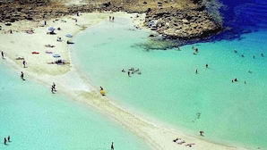 Una playa con agua turquesa cristalina, gente nadando y tomando el sol.