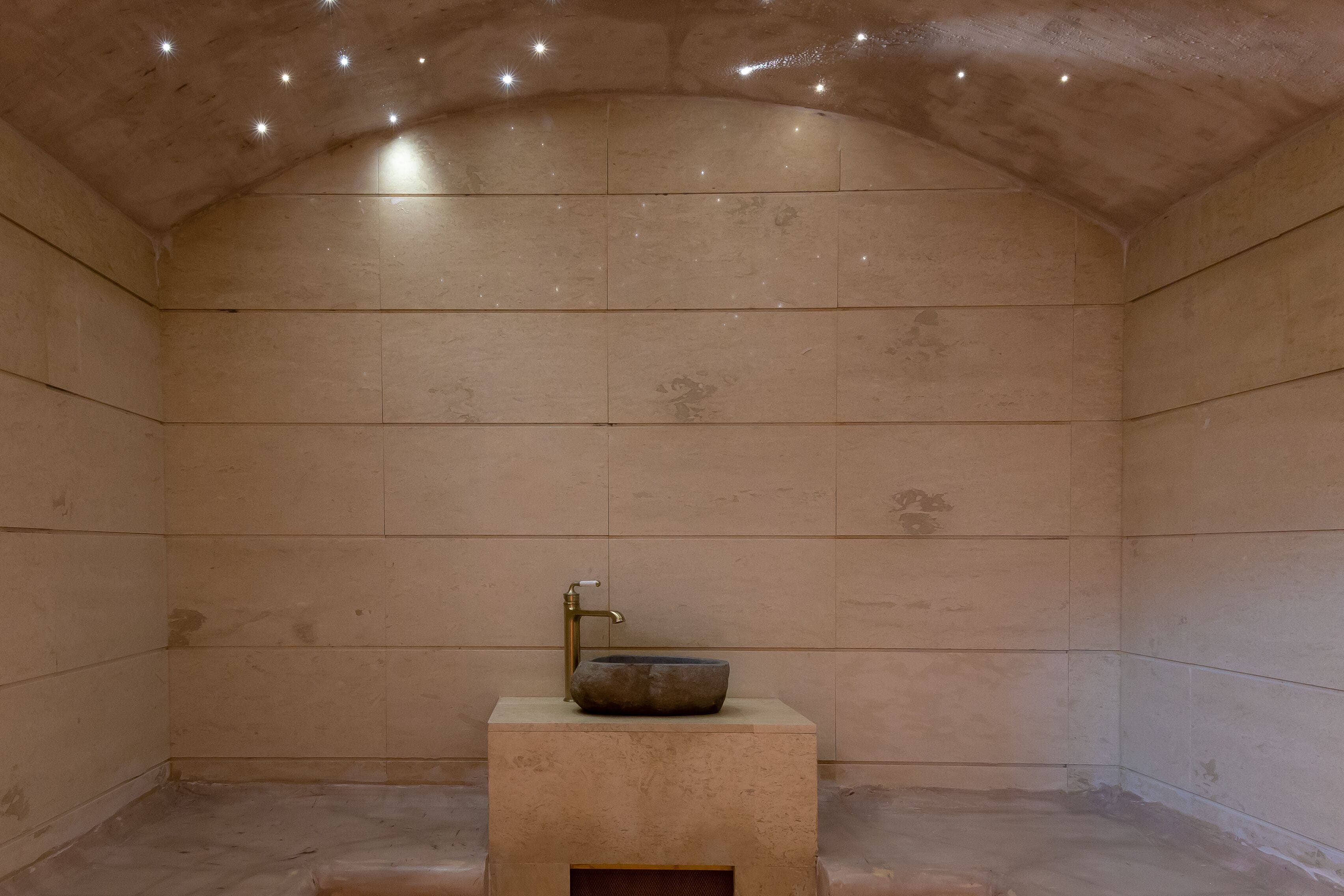 A bathroom with a stone sink on a pedestal, tiled walls, and a curved ceiling with recessed lighting.