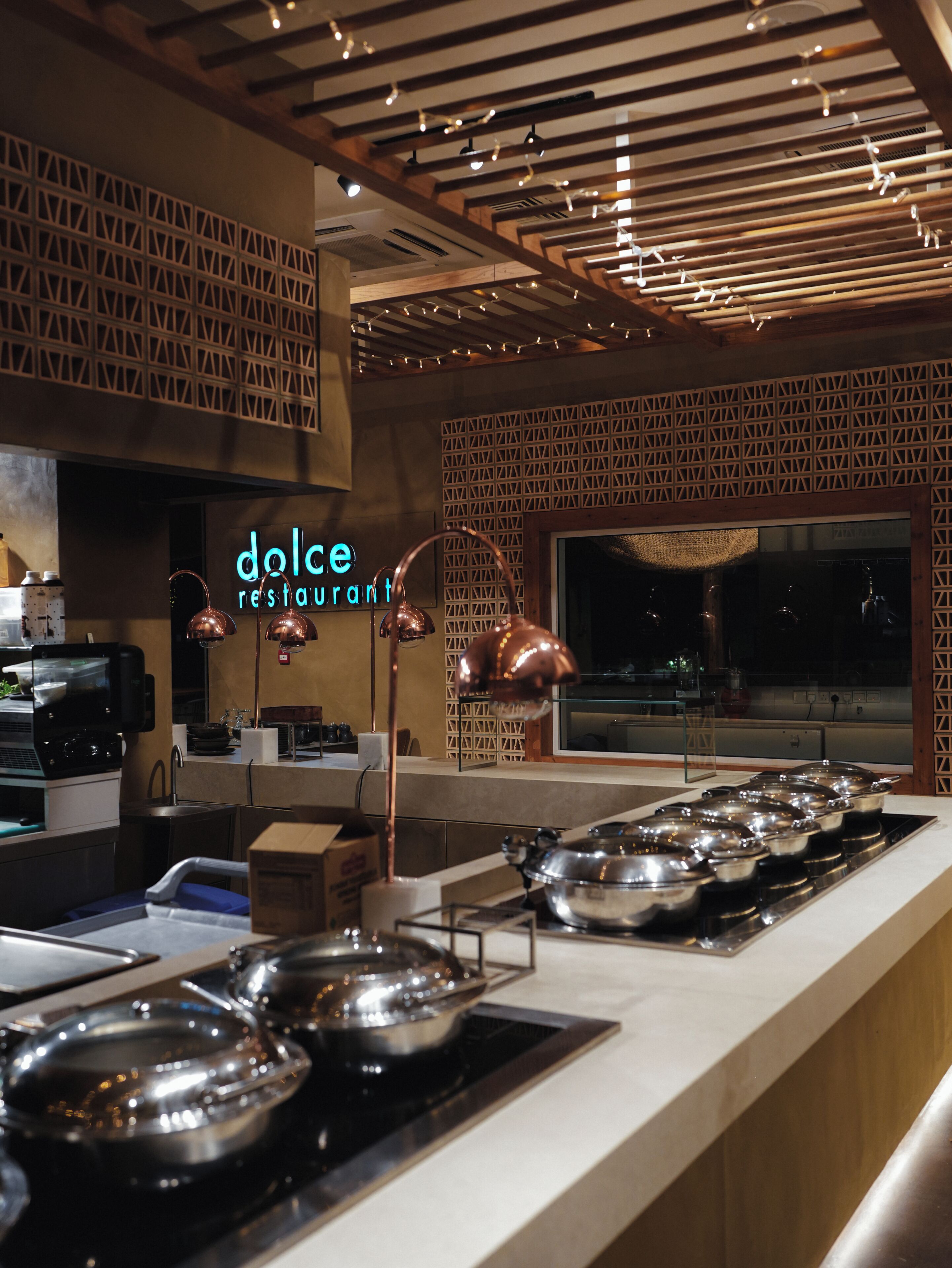 L’intérieur d’un restaurant, avec un comptoir où sont exposés différents plats, un panneau néon indiquant « dolce restaurant », et un mur orné de motifs.