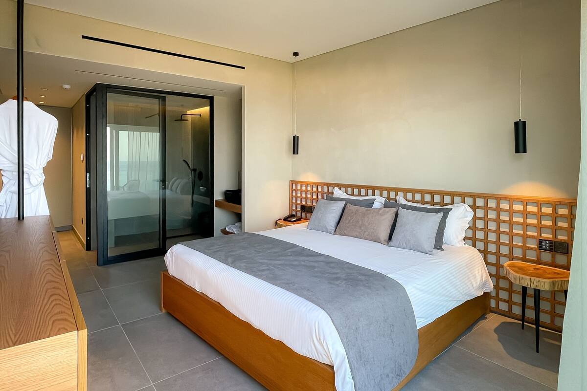 Ein Hotelzimmer mit einem Bett, einem Nachttisch aus Holz, einem Bademantel, einer Schiebetür zu einem Balkon und einem hölzernen Kopfteil.