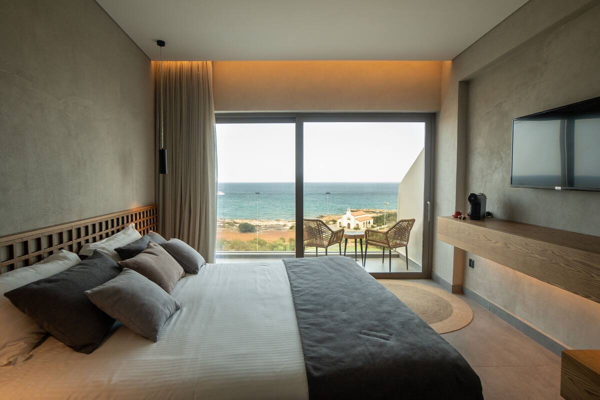 Ein Schlafzimmer mit einem großen Bett, einem Fernseher, einem Balkon mit Meerblick und einem Essbereich.