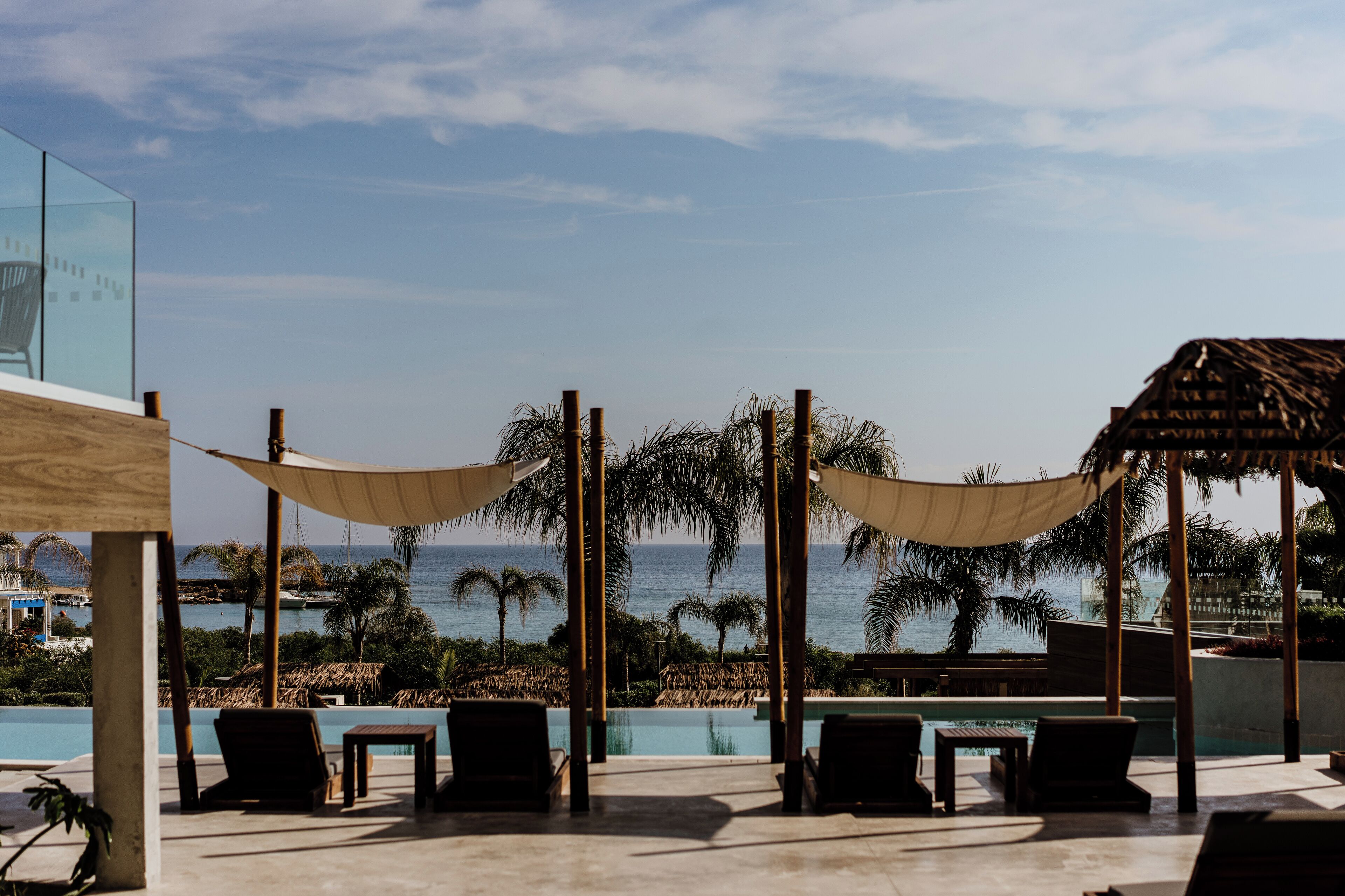 A poolside area with lounge chairs, a thatched-roof structure, and a view of the ocean.