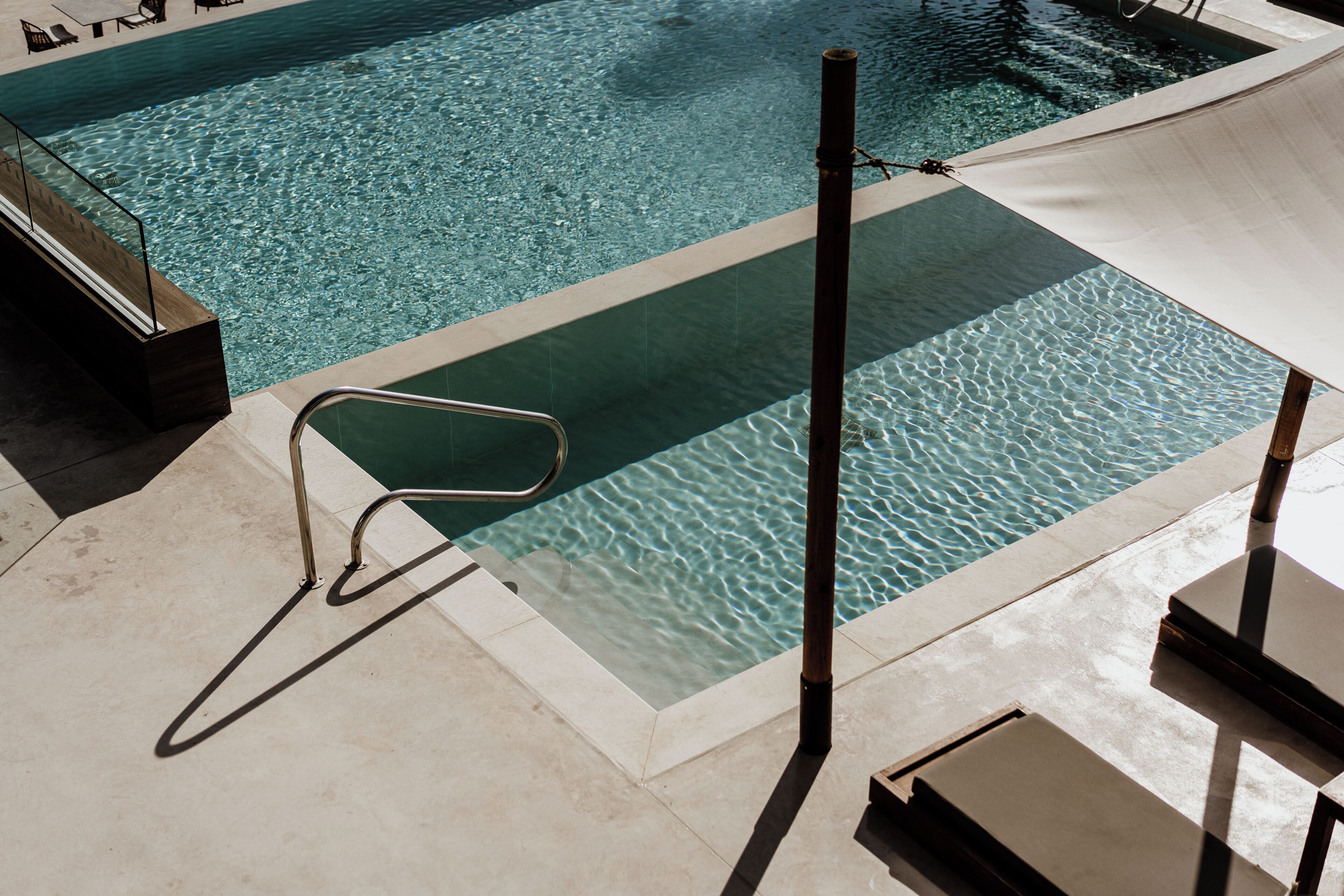 Une piscine à l’eau claire, une échelle en métal et un espace ombragé avec des chaises longues.