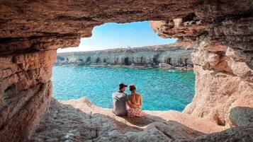 Una pareja sentada en un risco con vista al mar azul y despejado, con acantilados al fondo.