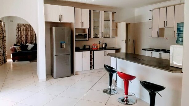 A compact kitchen with a refrigerator, microwave, and a water dispenser. There are two bar stools and a small dining table. - WestPoint Quays (Harare)