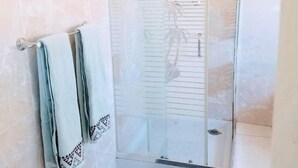 A glass-enclosed shower with a tiled floor and a doormat. - WestPoint Quays (Harare)