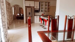 A modern kitchen with white cabinets, a microwave, and a dining area with red bar stools. - WestPoint Quays (Harare)