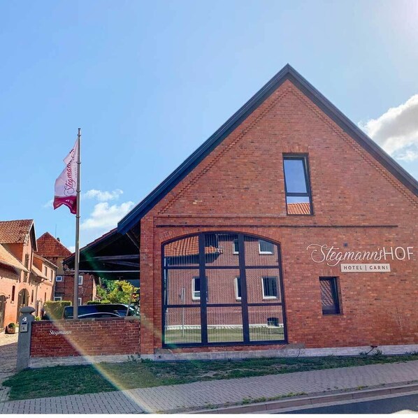 A brick building with a large arched entrance and a flagpole with a flag. The building has a sign that reads "Stegmann's Hof Hotel | Garni". - Hotel Stegmann's HOF (Sehnde)