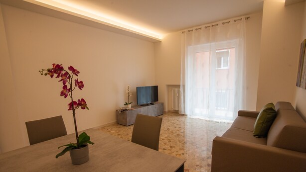 Una sala de estar moderna con una mesa de comedor, sillas, un sofá, un televisor y una orquídea en maceta.