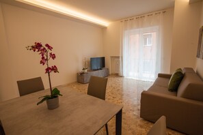 Una sala de estar moderna con una mesa de comedor, sillas, un sofá, un televisor y una orquídea en maceta.