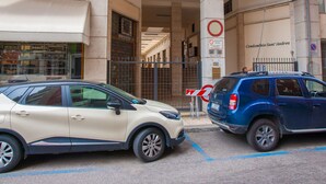 Un edificio con acceso cubierto, un cartel de no estacionamiento y dos coches aparcados al frente.