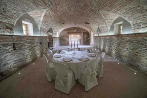Mesa redonda dispuesta para una comida en una habitación de paredes de piedra con techos abovedados y un ambiente rústico.