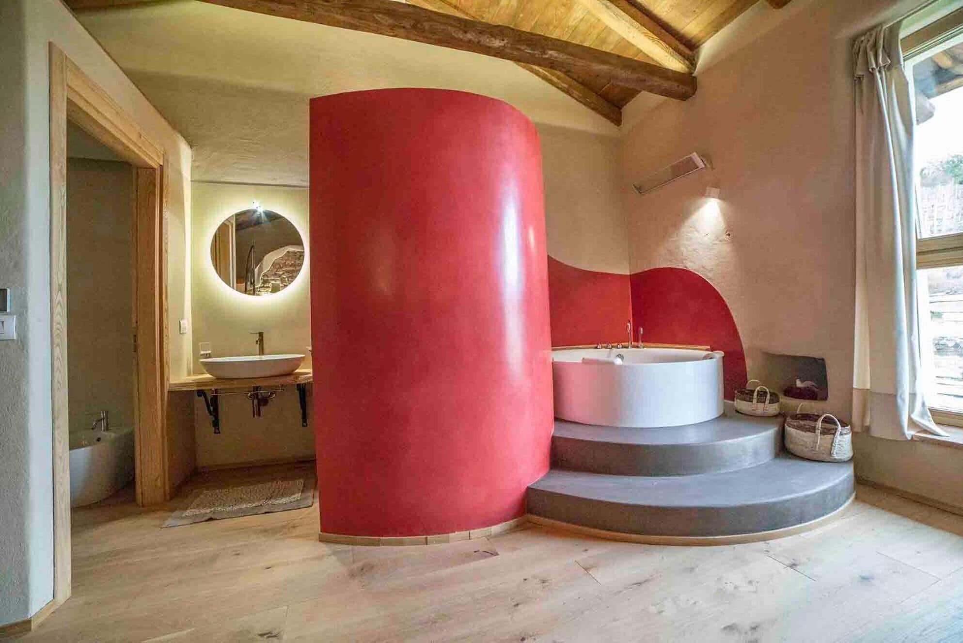 Un baño con un pilar rojo grande, un espejo redondo, un lavabo y una bañera.