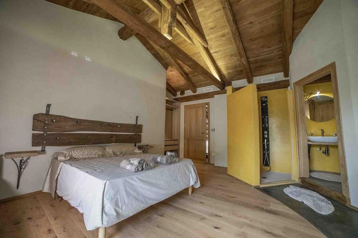 A bedroom with a wooden ceiling, a bed with a striped bedspread, a bench, and a wooden headboard.