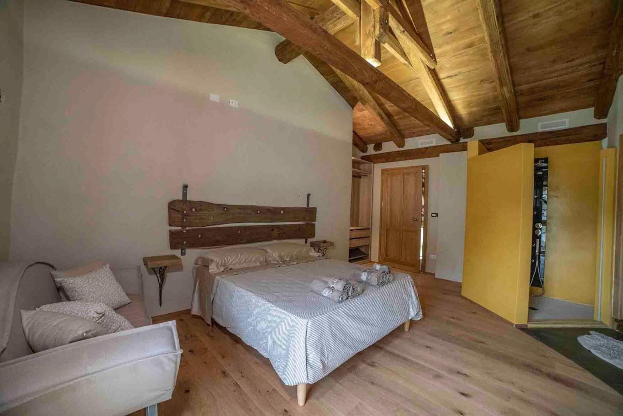 Un dormitorio con techo de madera, una cama con colcha a rayas, una silla y una mesita de noche.