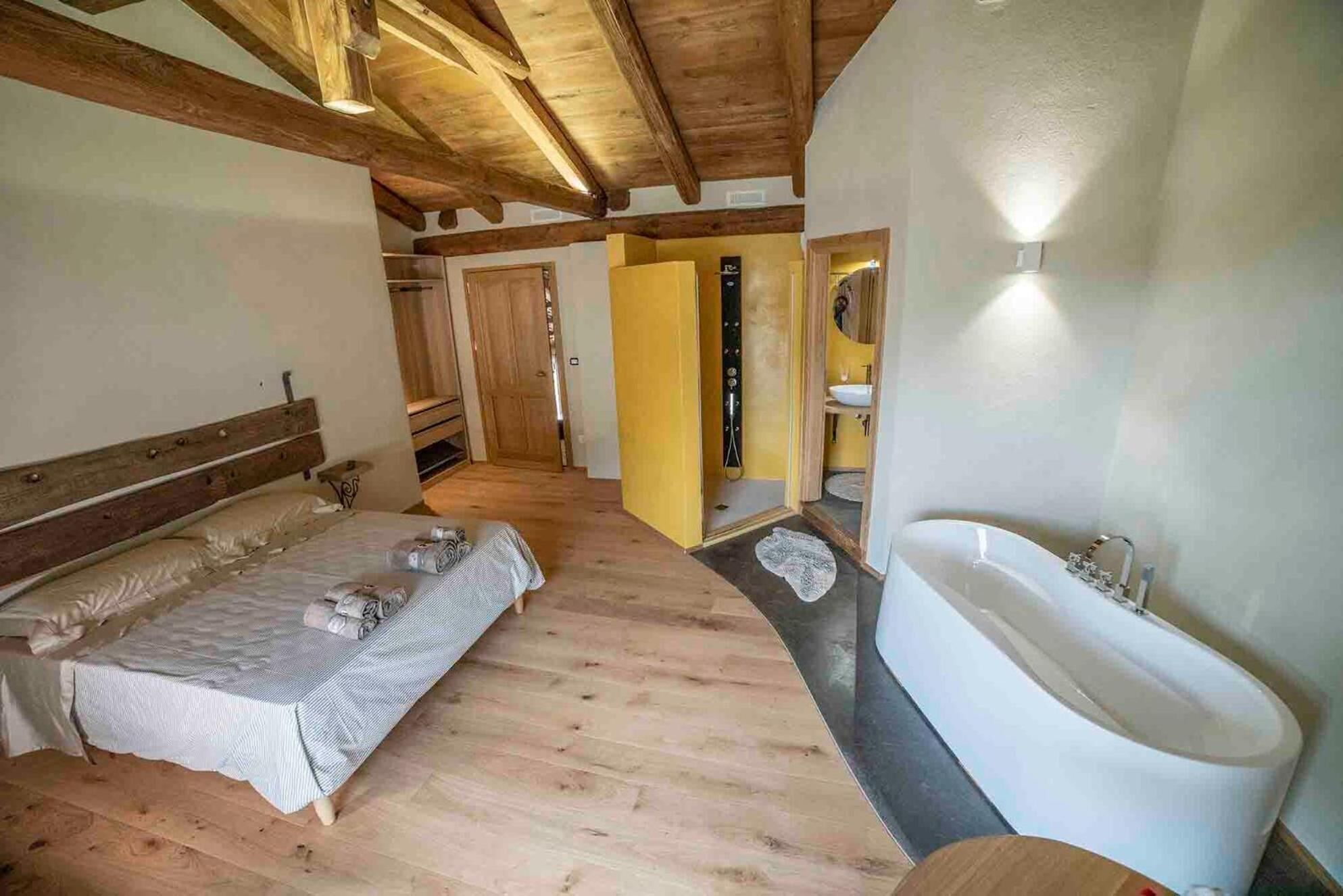 Una camera da letto con un letto grande, soffitto in legno e bagno con vasca e lavandino.