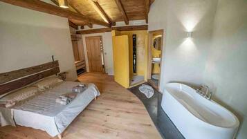 Una camera da letto con un letto grande, soffitto in legno e bagno con vasca e lavandino.