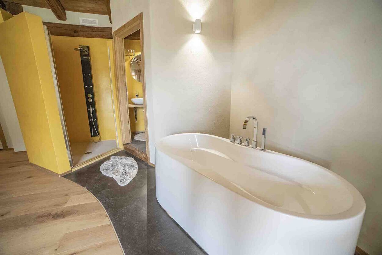 Un bagno moderno con una vasca freestanding, un pavimento in legno e una porta gialla che dà su un'altra stanza.