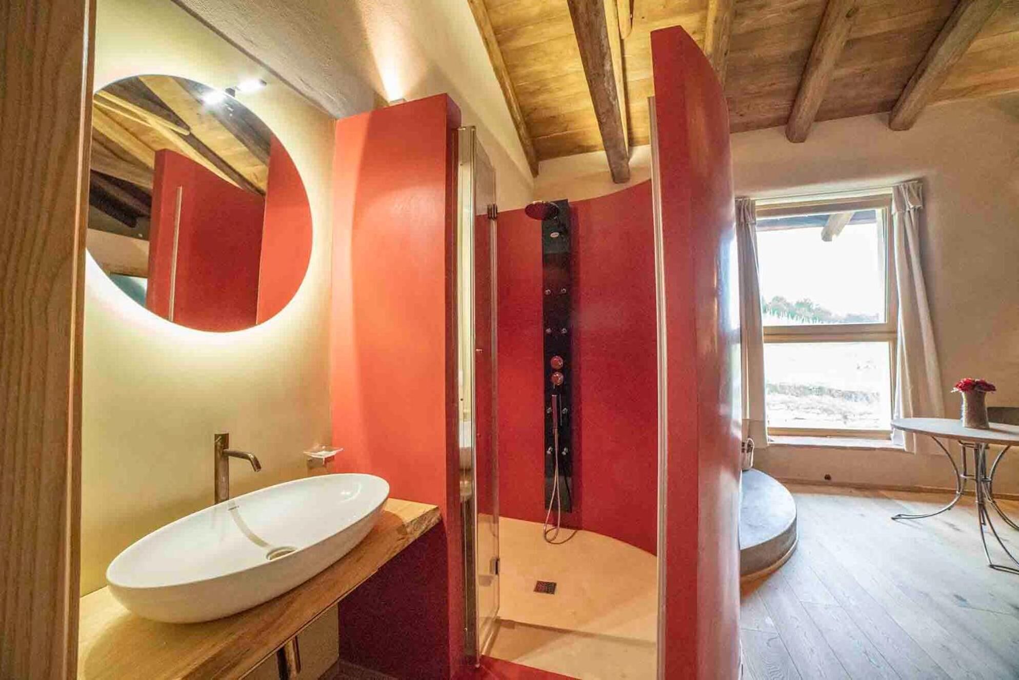 A bathroom with a large mirror, a white sink, and a red accent wall.