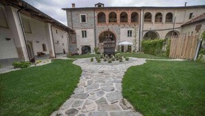 A courtyard with a stone pathway leading to a central fountain, surrounded by a building with arched windows and a tiled roof. - Tenuta Armonia (Clavesana)