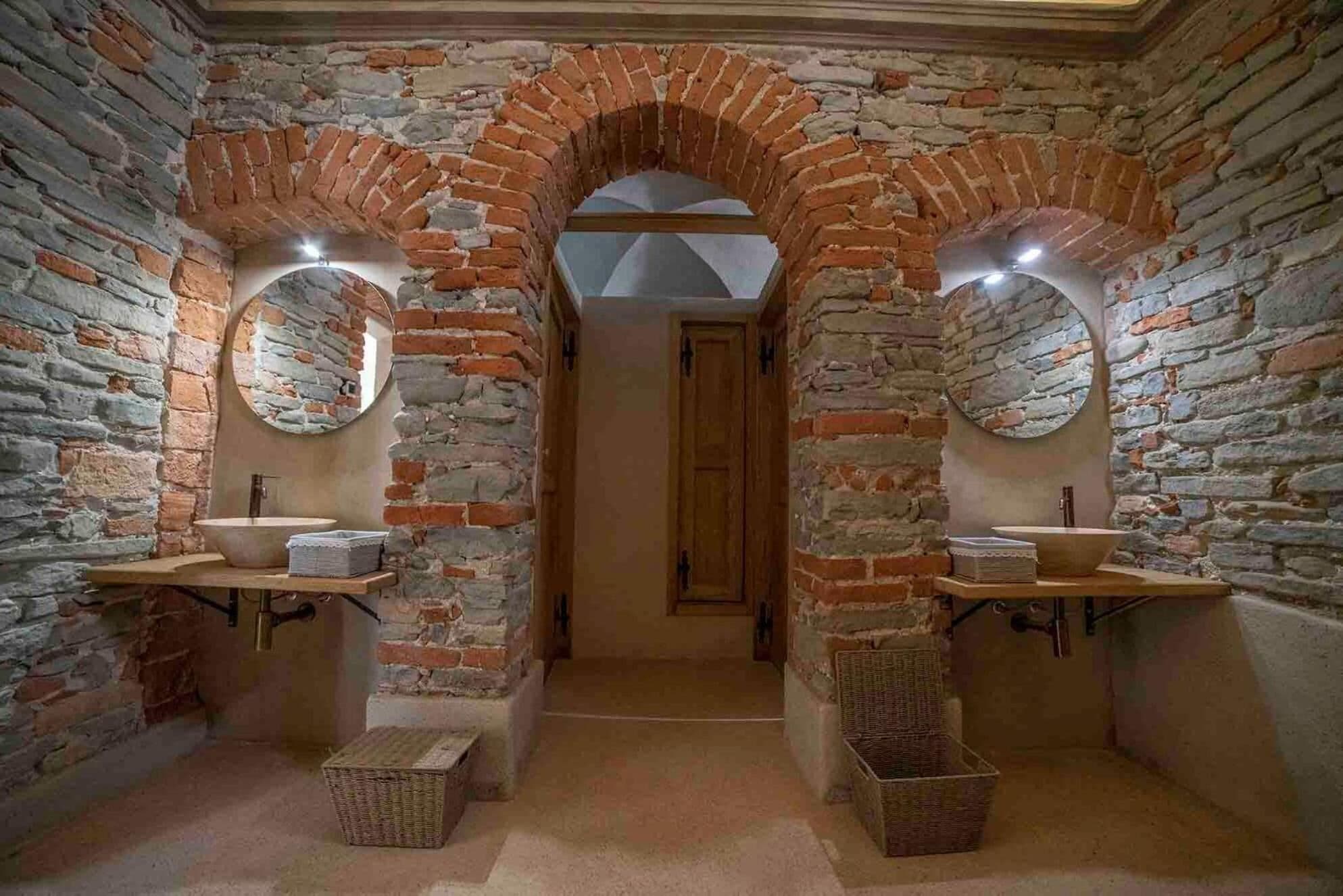 Un baño rústico con paredes de ladrillo, dos espejos redondos y una puerta de madera.