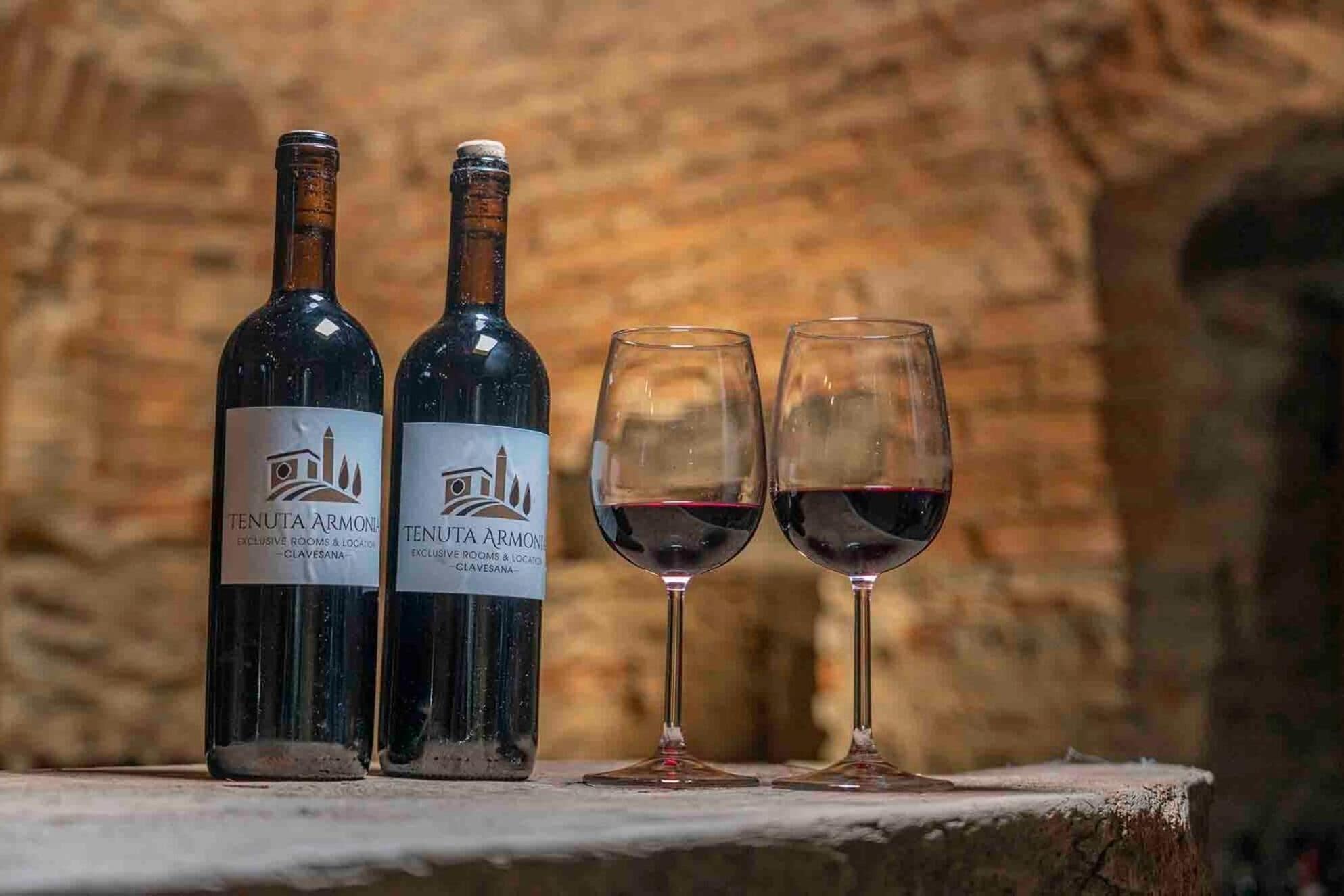 Deux bouteilles de vin Tenuta Armone et deux verres à vin sont posés sur une surface en pierre, avec un mur de briques en arrière-plan.