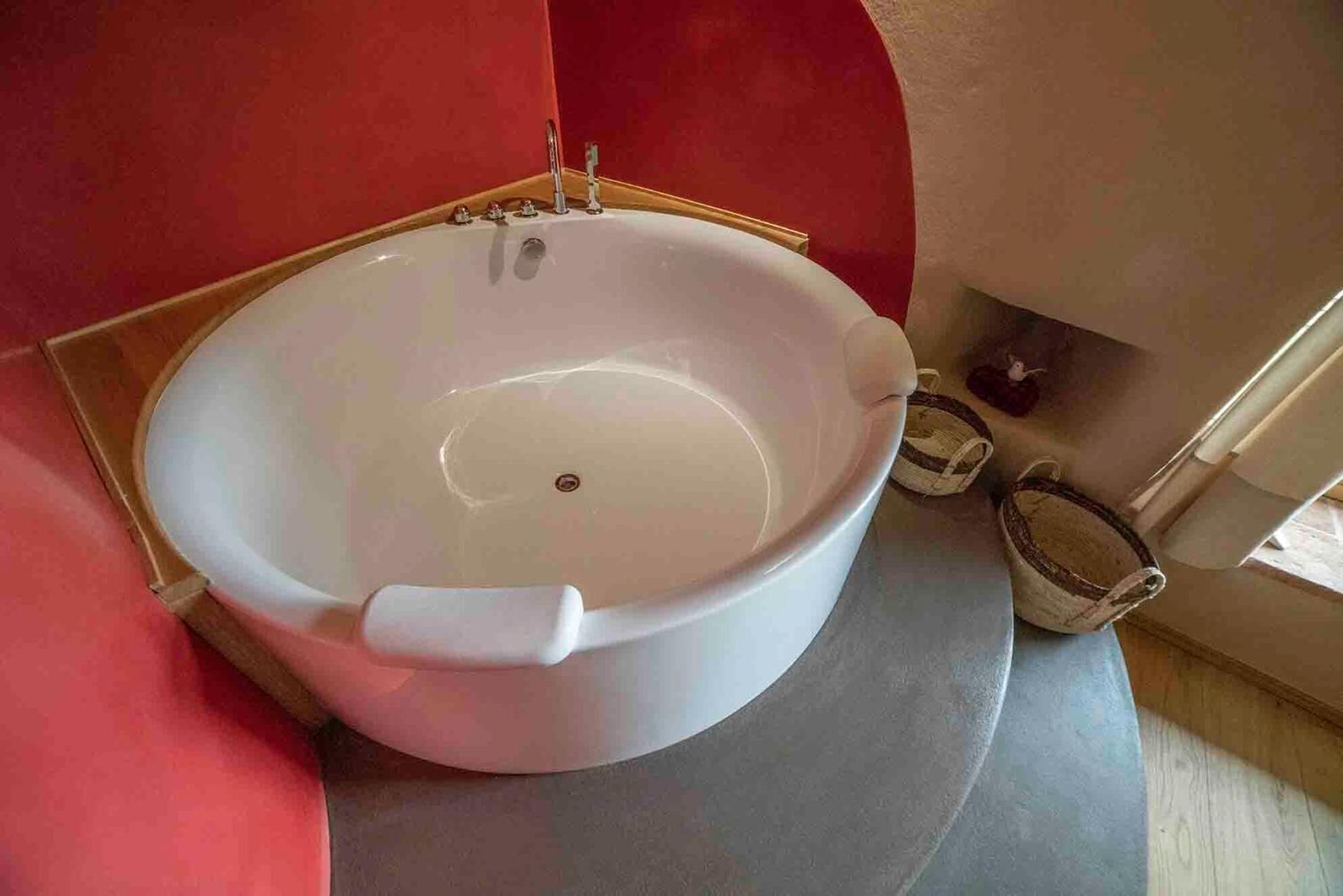 A large, round bathtub in a bathroom with a red wall and a wooden floor.