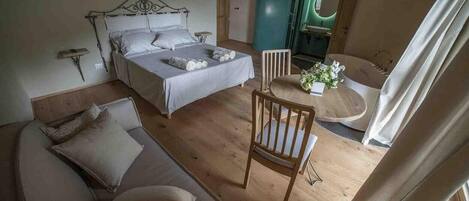 Un dormitorio con una cama, una silla de madera, un sofá y una mesita con un jarrón de flores.