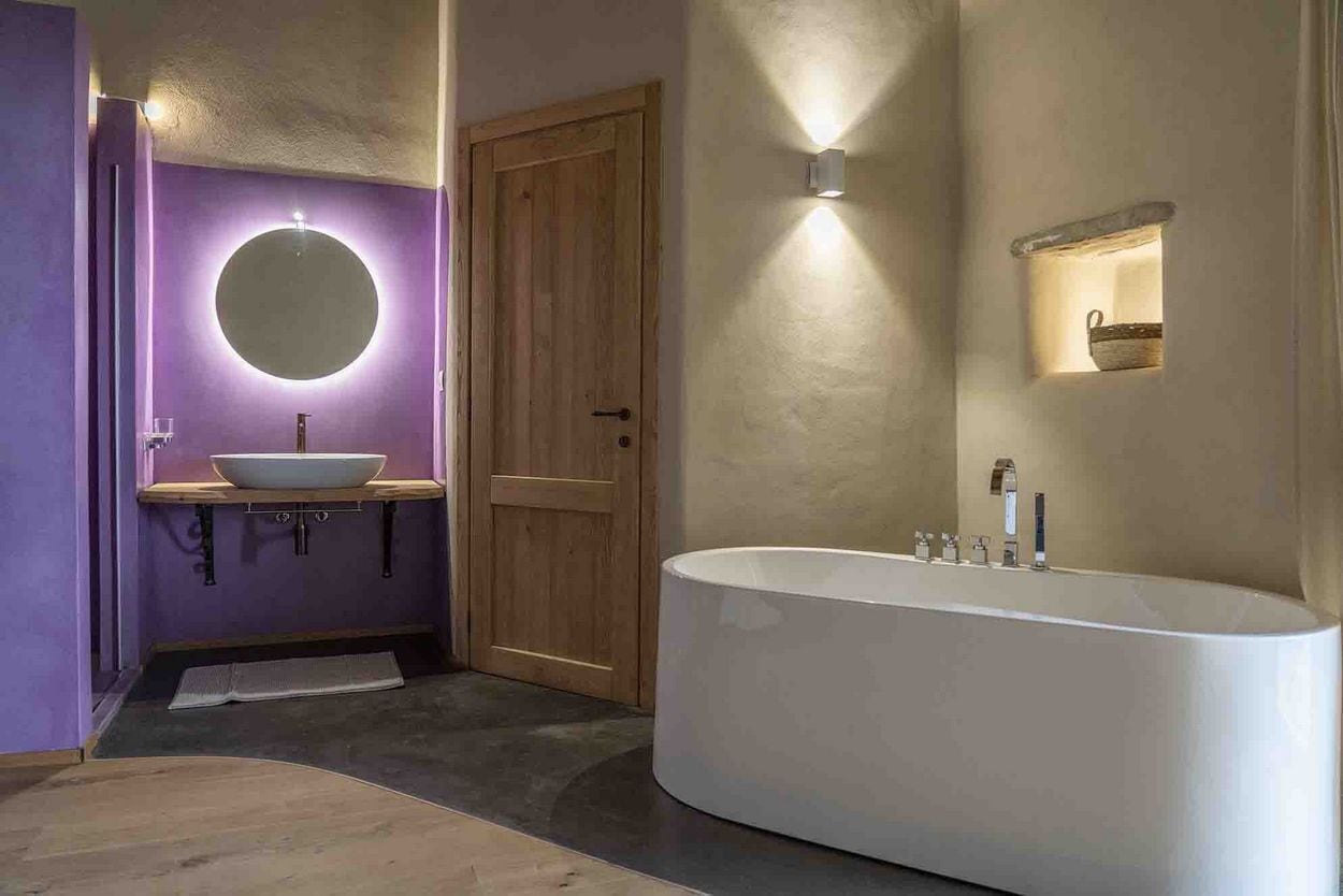 A modern bathroom with a freestanding bathtub, a round mirror, and a wooden door.