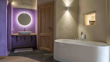 A modern bathroom with a freestanding bathtub, a round mirror, and a wooden door.