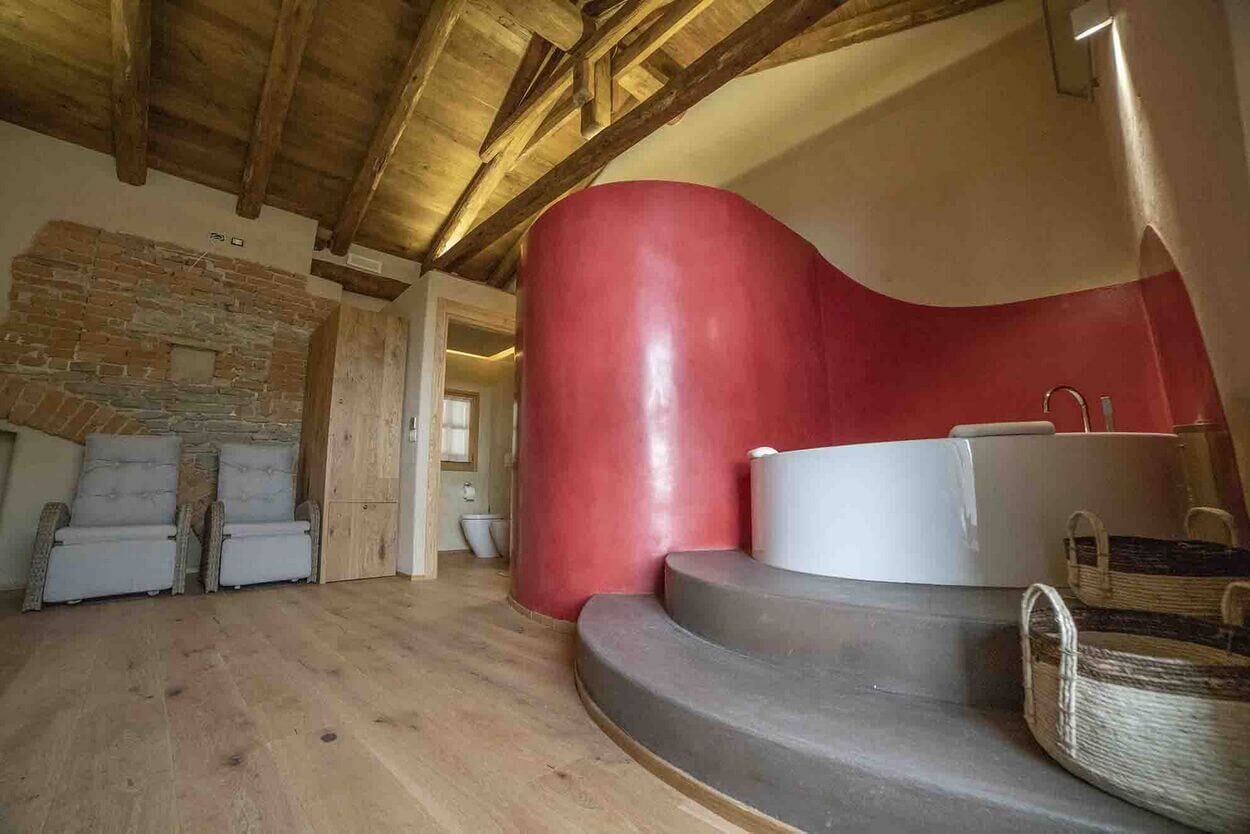 A room with a stone wall, wooden beams, a red cylindrical structure, a white bathtub, and wicker baskets.
