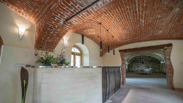 A spacious interior with a high, arched brick ceiling, a reception area with a counter, and a stone wall in the background. - Tenuta Armonia (Clavesana)