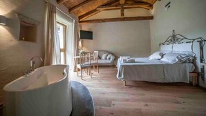 A bedroom with a wooden ceiling, a large bathtub, a bed with white bedding, and a chair. - Tenuta Armonia (Clavesana)