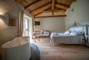 Un dormitorio con techo de madera, una bañera grande, una cama con ropa de cama blanca y una silla.