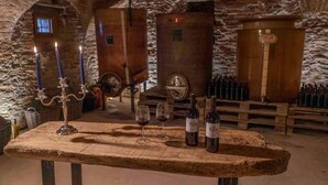 A rustic cellar with wooden barrels, a candelabra, and wine bottles on a table. - Tenuta Armonia (Clavesana)