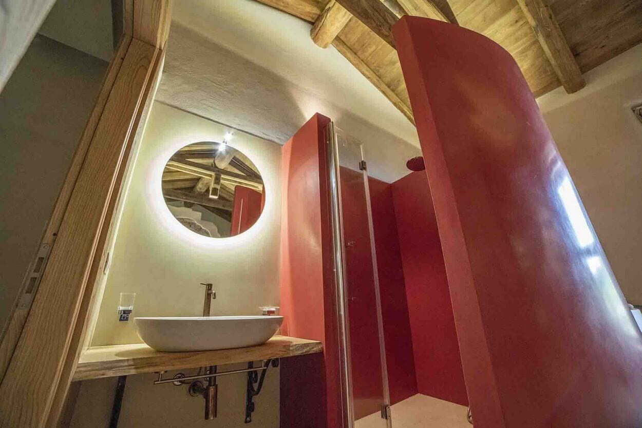 Un baño moderno con techo de madera, espejo redondo, lavamanos blanco y cabina de ducha con mampara de vidrio.