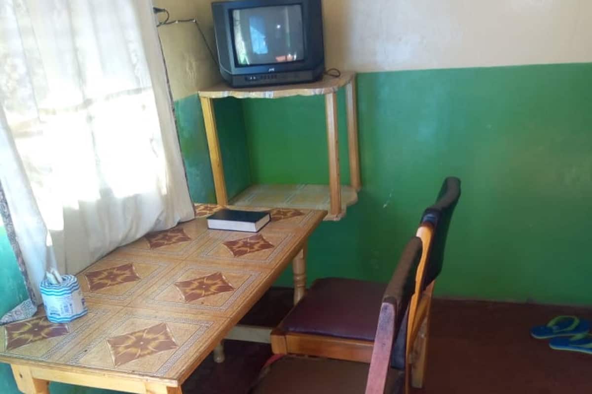Ett rum med ett träbord, en enda stol, en tv på ett stativ och en gardin.