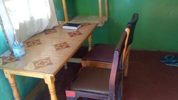 Una habitación con una mesa de madera, una silla, un televisor sobre un mueble y una cortina.