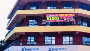 Un edificio de varios pisos con un letrero que indica 'Terrace Wedge Villa Kuku Point' y 'FamilyBank' en la planta baja.