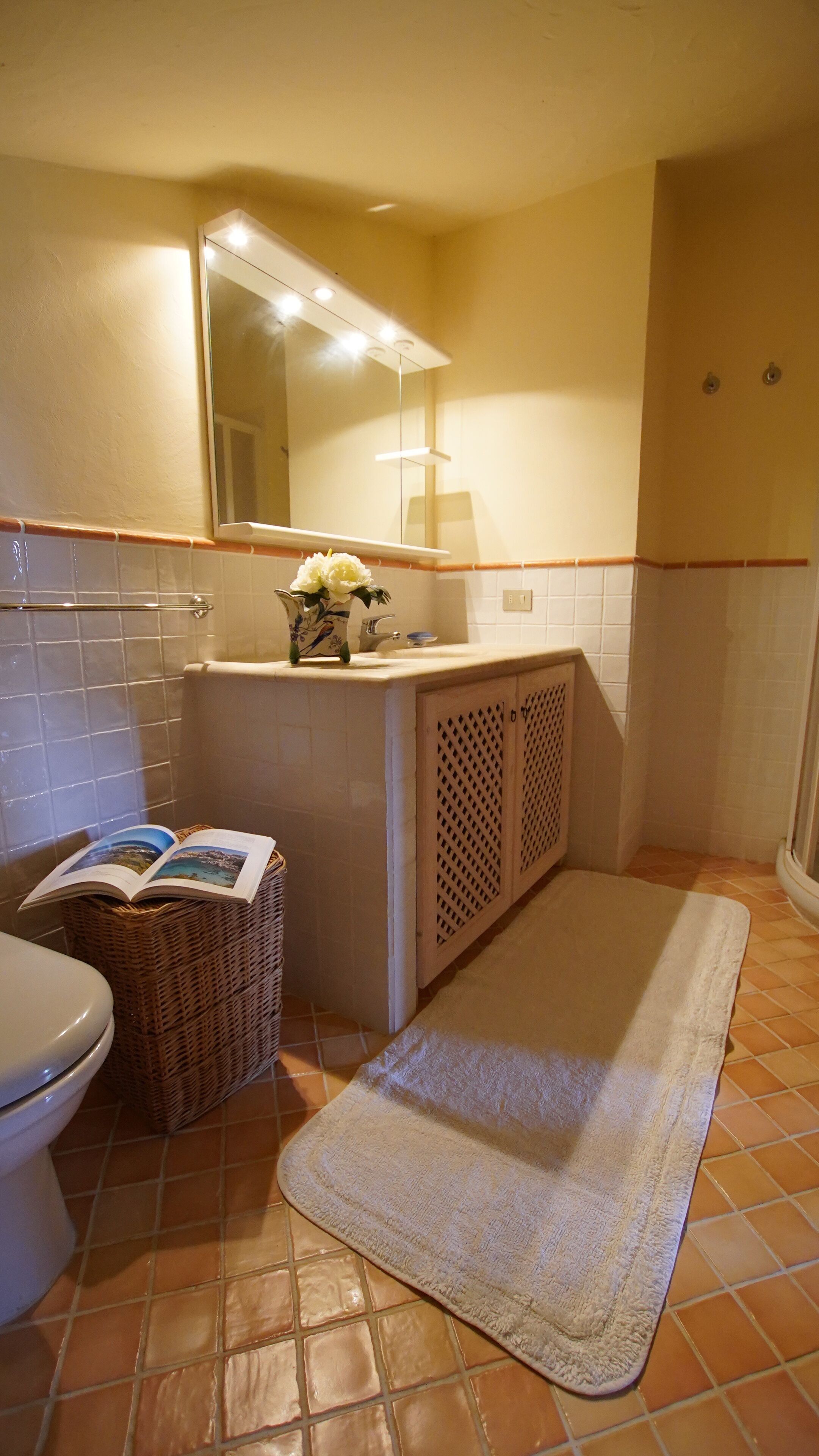 A bathroom with a toilet, a sink with a mirror above it, a wicker basket, and a towel on the floor.