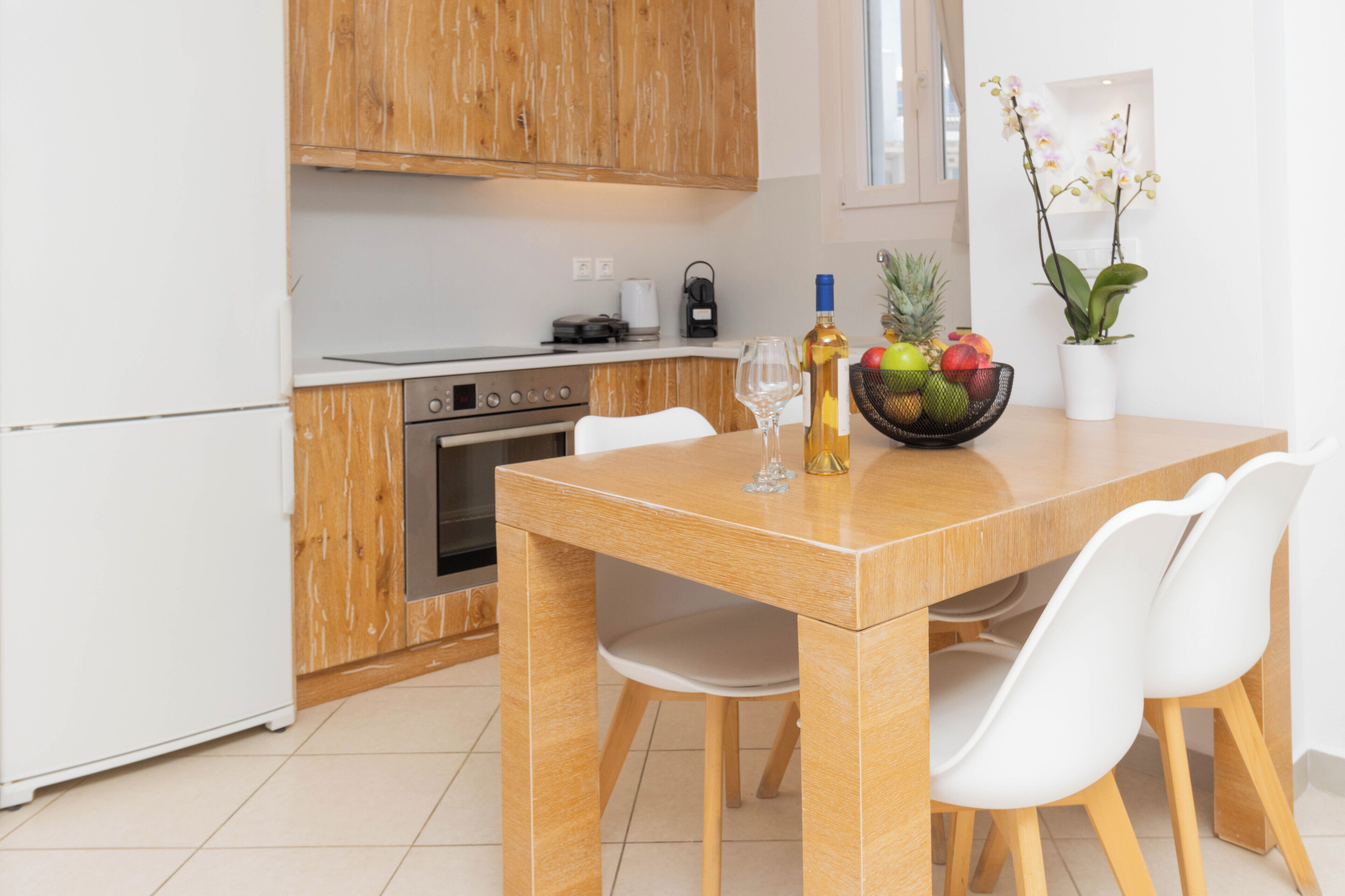 Une cuisine moderne avec des meubles en bois, un four en acier inoxydable et une table à manger avec des chaises blanches.