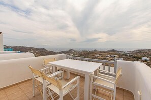 A terrace with a table and chairs, overlooking a coastal landscape with white buildings.
