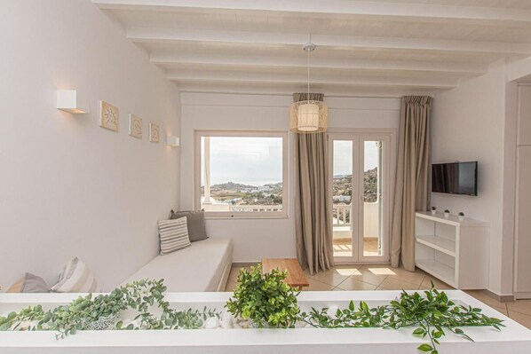 A modern living room with a sofa, a dining table, a TV, and a view of the city through large windows.