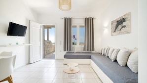 Un salon moderne avec un canapé, un téléviseur fixé au mur et une vue sur l’extérieur grâce à de grandes fenêtres.