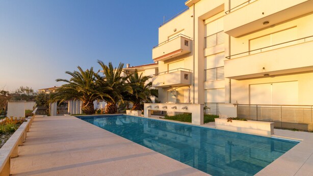 Ein modernes Gebäude mit Pool, Palmen und blauem Himmel.