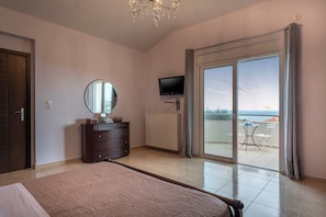 A bedroom with a bed, a dresser, a TV, and a sliding glass door leading to a balcony with a view. - Villa Familia Chania (Chania)