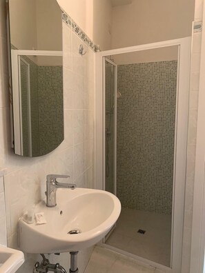 Un baño con un lavabo blanco, un espejo y una ducha con mosaicos.