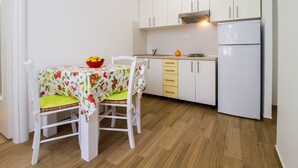 Eine kleine Küche mit weißen Schränken, einem weißen Kühlschrank und einem Tisch mit Obstschale.
