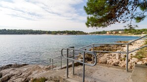 Eine Küstenansicht mit einer Betonstiege, die zu einem Sandstrand führt, mit Blick auf ein ruhiges Meer.