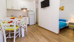 Ein gemütlicher Raum mit Küchenzeile, einem Essbereich mit Tisch und Stühlen, einem Bett mit blauer Bettdecke und einem an der Wand montierten Fernseher.
